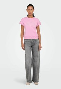 Roze sweatshirt met de tekst "GOOD VIBES", korte mouwen en ribgebreide zoom, gecombineerd met grijze wijde jeans en beige textuur schoenen.