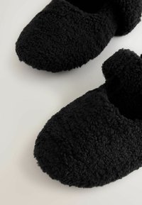 Pantofole nere e pelose realizzate in materiale morbido e strutturato. Design chiuso con punta arrotondata e copertura accogliente per la caviglia.