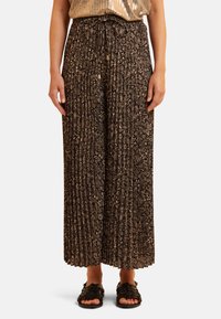Zwarte geplooide broek met een bloemenpatroon in goudtinten, voorzien van een elastische tailleband en een wijde pijp, gecombineerd met zwarte sandalen.