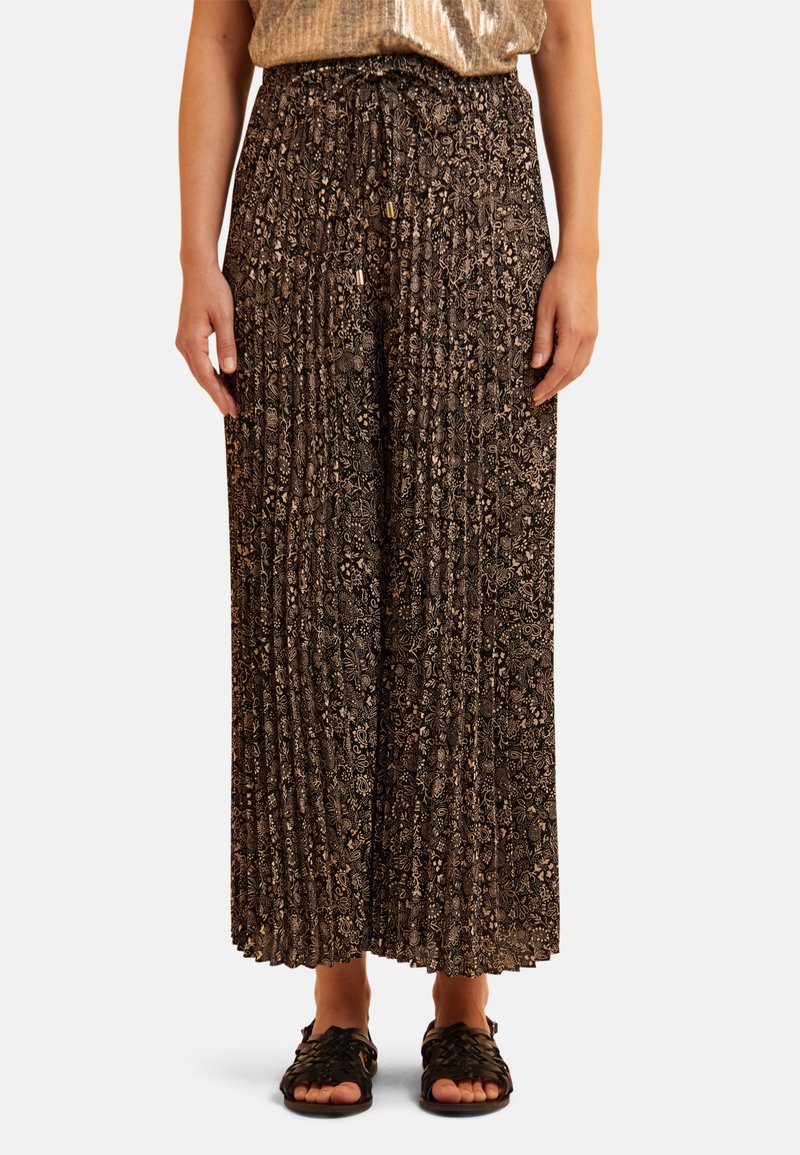 Zwarte geplooide broek met een bloemenpatroon in goudtinten, voorzien van een elastische tailleband en een wijde pijp, gecombineerd met zwarte sandalen.