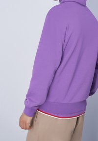 Sudadera púrpura con un corte relajado, puños y dobladillo acanalados. Con un detalle de rayas rojas y blancas en la parte inferior. Material suave.