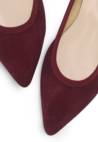 Burgunderfarbene Wildleder-Pumps mit spitzem Zehenbereich; elastischer Rand; glatte, nude-farbene Innensohle; elegantes, minimalistisches Design. Keine sichtbaren Beschläge oder Muster.