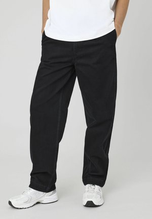 Pantalons en coton noir avec une coupe décontractée, dotés de poches latérales et d'une texture lisse. Associés à des baskets blanches.