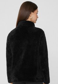 Czarna kurtka z sztucznego futra z wysokim kołnierzem, długimi rękawami i miękką, teksturowaną powierzchnią. Posiada swobodny krój i gładkie wykończenie.