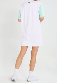 Biała bawełniana sukienka t-shirtowa z miętowo-zielonymi krótkimi rękawami i logo FILA na tylnej szyi. Luźny krój i długość do połowy uda.