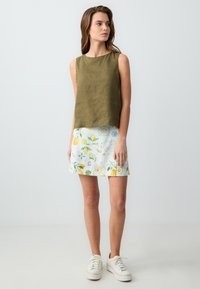 Top senza maniche in lino verde oliva abbinato a una gonna bianca con motivi floreali gialli di limone e blu, completato da sneakers chiare.