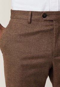 Braune Fischgrät-Hosen mit glatter Textur, ausgestattet mit einem einzelnen Knopfverschluss und seitlichen Taschen für Funktionalität.