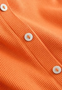 Tissu côtelé orange avec trois boutons blancs cousus au fil orange en ligne verticale.