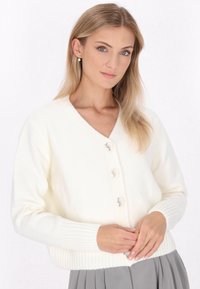 Biała, dziana kardigan z dekoltem w kształcie V, prążkowanymi mankietami oraz zapinaniem na guziki z przodu z czterema jasnymi guzikami. Gładka tekstura i klasyczny krój.