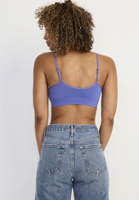 Lila stretch-bh med justerbara axelband som visar en slät textur. Bärs med högmidjade ljusblå jeans i denim som har bakfickor.
