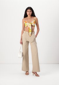 Top floreale corto con nodo frontale, caratterizzato da motivi gialli, arancioni e verdi. Abbina con pantaloni larghi beige e borsa bianca.