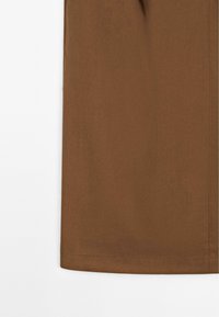 Tissu marron avec un détail de couture droite près du bord sur un fond blanc.
