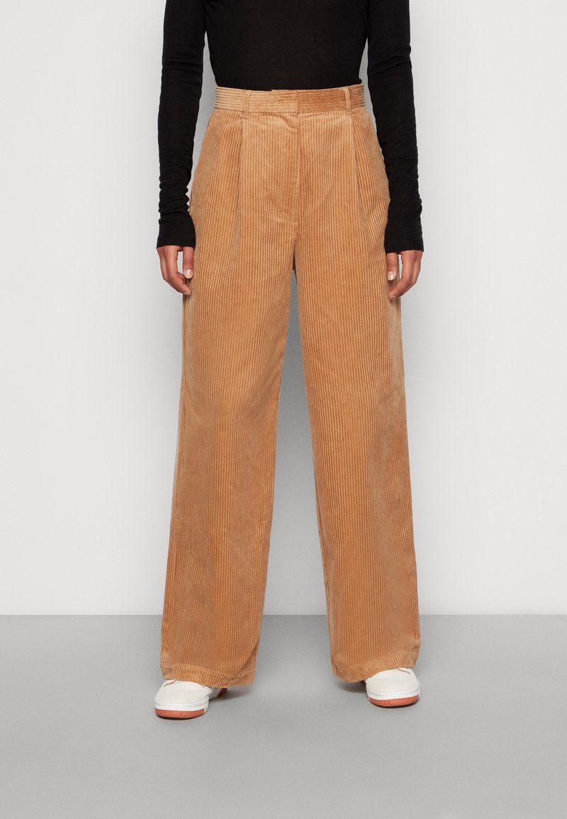 Beige kordflorsbyxor med vida ben och vertikala ränder, hög midja och framfållar. Kombinerat med vita sneakers.