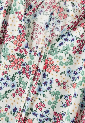 Kwiatowa bluzka z lekkiego materiału, z mieszanką czerwonych, różowych, niebieskich i zielonych kwiatów na białym tle, z zawiązywanym dekoltem.