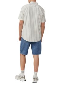 Helles gestreiftes Kurzarmhemd kombiniert mit Jeansshorts. Das Hemd ist cremefarben mit grünen Streifen; die Shorts sind klassisches blaues Denim. Weiße Turnschuhe runden das Outfit ab.