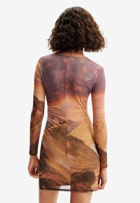 Robe courte à manches longues avec un imprimé paysager aux tons terreux, texture lisse et coupe ajustée, mettant en valeur des nuances et textures en dégradé.