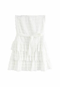 Robe blanche à niveaux fabriquée en tissu texturé, présentant un corsage smocké et une ceinture nouée à la taille. Les couches ont des bords froncés.