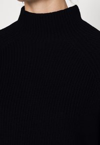 Schwarzer gerippter Strickrollkragenpullover mit hohem Kragen, der eine strukturierte Oberfläche und ein nahtloses Schulterdesign aufweist. Keine sichtbaren Beschläge oder Akzente.