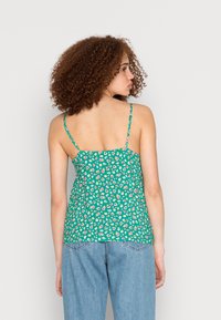 Top de alças finas verde com padrão floral, apresentando um corpete ajustado e uma bainha cascata, feito de tecido leve com um padrão texturizado.