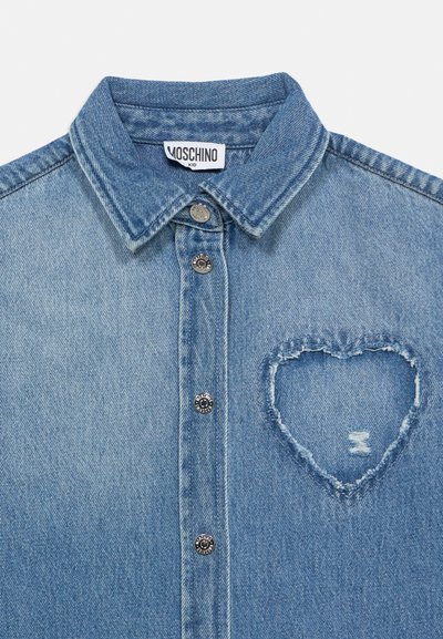 Chemise en denim à boutons avec col, comportant un patch usé en forme de cœur sur la poitrine et une étiquette Moschino Kid à l'intérieur du col.