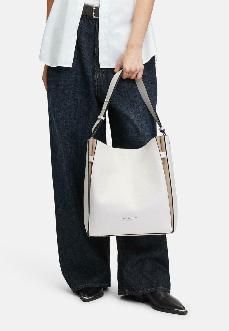 Sac seau en cuir blanc avec des accents gris et une texture lisse. Présente des ferrures en argent et un logo sur le devant. Forme arrondie.