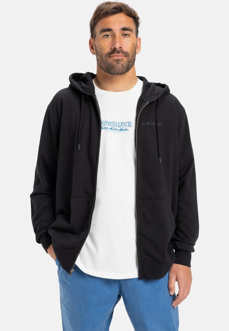 Fleeced hoodie preto com fecho, com capuz ajustável, feito de tecido macio, emparelhado com uma t-shirt branca com texto e imagem azuis, e calças azuis.