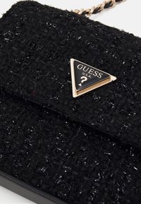 Borsa a mano nera con texture che presenta un logo triangolare lucido di Guess in oro e nero, dotata di una tracolla a catena e un design in tessuto intrecciato.