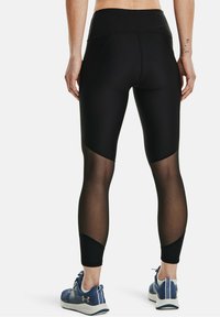 Czarne legginsy z wysokim stanem, z przezroczystymi panelami bocznymi i dopasowanym krojem. W komplecie z niebieskimi butami sportowymi.