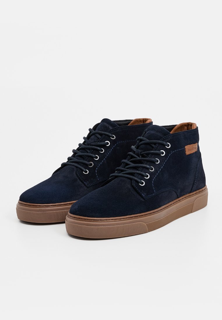 Marineblaue Wildleder-Hochtop-Schuhe mit Schnürdesign, kontrastierender brauner Gummisohle und braunem Lederelement am Knöchel. Strukturierte Oberfläche.