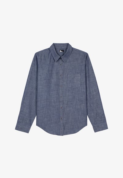 Camisa de manga longa em chambray azul com colarinho abotoadurado, bolso frontal e fecho por botões, apresentando uma textura lisa e bainha arredondada.
