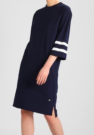 Vestido azul marino con mangas cortas y anchas que presentan dos franjas blancas. El vestido tiene un escote de cuello redondo y aberturas laterales para facilitar el movimiento.