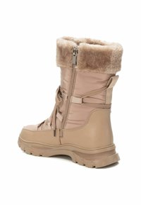 Botín de invierno beige con caña acolchada, puño de piel sintética, cremallera lateral y cordones en el frontal. Suela de goma con textura para mayor agarre.