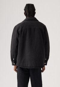 Černá džínová bunda s volným střihem, zapínáním na knoflíky na manžetách a detailem na zadním lyku. Jednoduchý design, texturovaná tkanina, dobře zpracované švy.