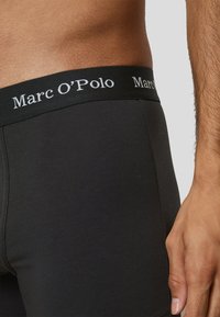 Boxer da uomo neri con una texture liscia, dotati di una ampia vita nera con il logo "Marc O'Polo" in lettere bianche in rilievo.
