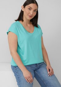 Turquoise T-shirt met korte mouwen en V-hals, gemaakt van zacht, lichtgewicht materiaal, gecombineerd met een blauwe spijkerbroek, weergegeven op een neutrale achtergrond.