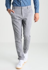 Gray, tailored trousers in a textured fabric with a slim fit, featuring side pockets and a flat front, paired with white sneakers.