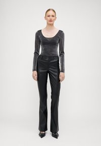 Schwarze Kunstlederhosen mit leichtem Schimmer, kombiniert mit einem figurbetonten, schimmernden dunkelgrauen Langarmoberteil mit Rundhalsausschnitt.