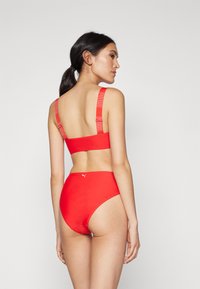 Červený bikini set s bandeau topom a logovými popruhmi, vysokými nohavičkami. Hladká textúra a minimalistický dizajn s športovým vzhľadom.