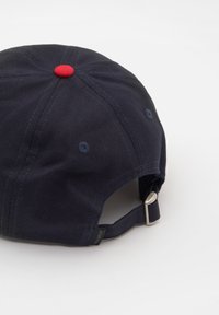 Marineblaue Kappe aus strukturiertem Stoff, mit einem roten Knopfakzent oben, einem verstellbaren Riemen hinten und Belüftungsöffnungen.
