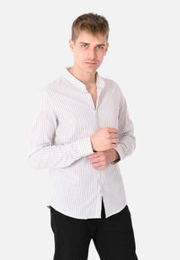 Camicia leggera a maniche lunghe con bottoni, in un motivo a righe bianche e azzurro chiaro. Presenta un colletto a banda e un orlo curvo. Indossati pantaloni neri.