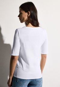 T-shirt blanc ajusté à manches trois-quarts, col rond et texture en coton lisse, associé à un jean en denim bleu.