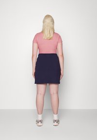 Tričko s krátkým rukávem, světle růžové, přiléhavého střihu, zkombinované s tmavě modrou sukní s elastickým pasem a teniskami s šedými a bílými akcenty.