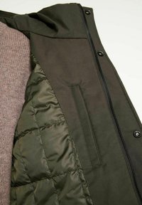 Olivgrön jacka med en kviltad innerfoder och dragkedjestängning. Inkluderar en bröstficka och en mjuk, strukturerad stickad insida.