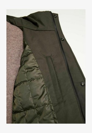 Olivengrüne Jacke mit wattiertem Innenfutter und Reißverschluss. Enthält eine Brusttasche und ein weiches, strukturiertes Strickfutter.