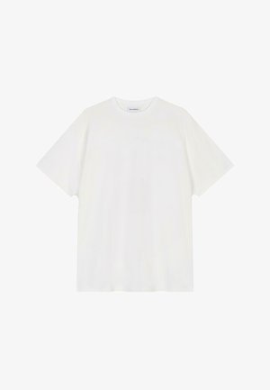 Balta kokvilnas T-kreklā ar īsām piedurknēm, apaļu kakla izgriezumu un brīvu piegriezumu; gluda tekstūra bez rakstiem vai rotājumiem.