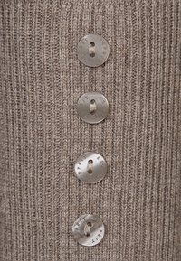 Quatre boutons translucides avec le texte « Esprit » alignés verticalement sur un tissu côtelé beige en maille.
