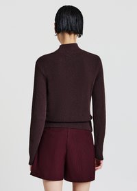 Dunkelbrauner, strukturierter Pullover mit hohem Kragen, langen Ärmeln und einem taillierten Saum, kombiniert mit burgunderroten Shorts mit Nadelstreifen.