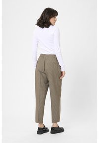 Witte lange mouwen shirt gecombineerd met bruine geruite broek met een hoge taille en voorzakken, aangevuld met zwarte schoenen.