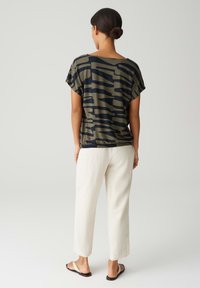 Donkergroen top met marineblauw abstract patroon, losse pasvorm, korte mouwen; gecombineerd met lichte, losse broek en sandalen.