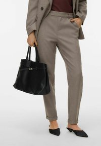 Persona che indossa pantaloni beige su misura, una maglietta scura, tiene una borsa in pelle nera e indossa sabot neri a punta con tacco basso.